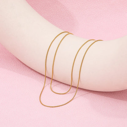 a gold necklace displayed on a pink background