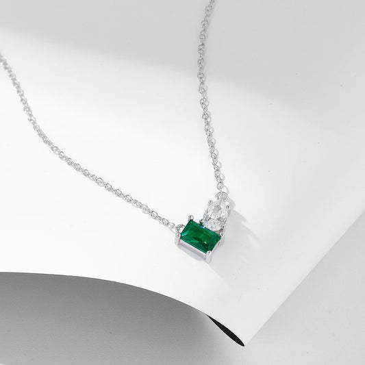 a silver necklace with green and white gemstones on a white surface