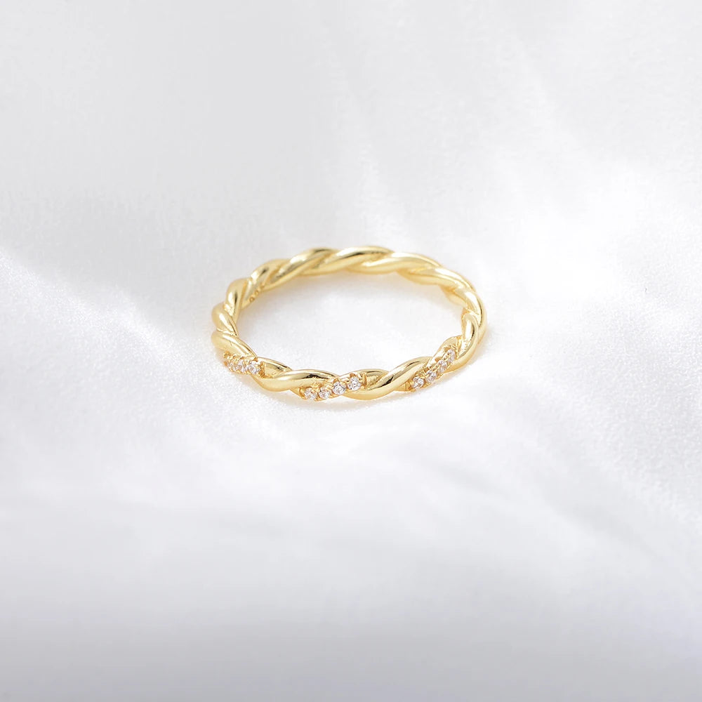 a gold twisted ring with sections of gemstones on it laying on a white surface
